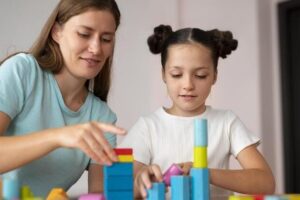 Sessao Terapia Aba Profissional conduz sessão de terapia ABA com criança utilizando blocos coloridos para estimular o desenvolvimento cognitivo e social.