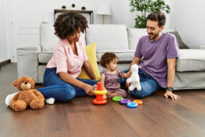 como lidar com autismo no dia a dia Pais brincando com uma criança pequena no chão da sala, utilizando brinquedos educativos coloridos.