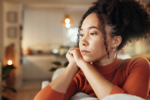 psicoterapia para ansiedade Mulher sentada em casa, com expressão pensativa, apoia o rosto nas mãos em um ambiente acolhedor e silencioso.