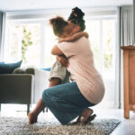 Mãe abraçando a filha em um ambiente doméstico, representando acolhimento, afeto e a importância do cuidado emocional diante da sobrecarga materna.