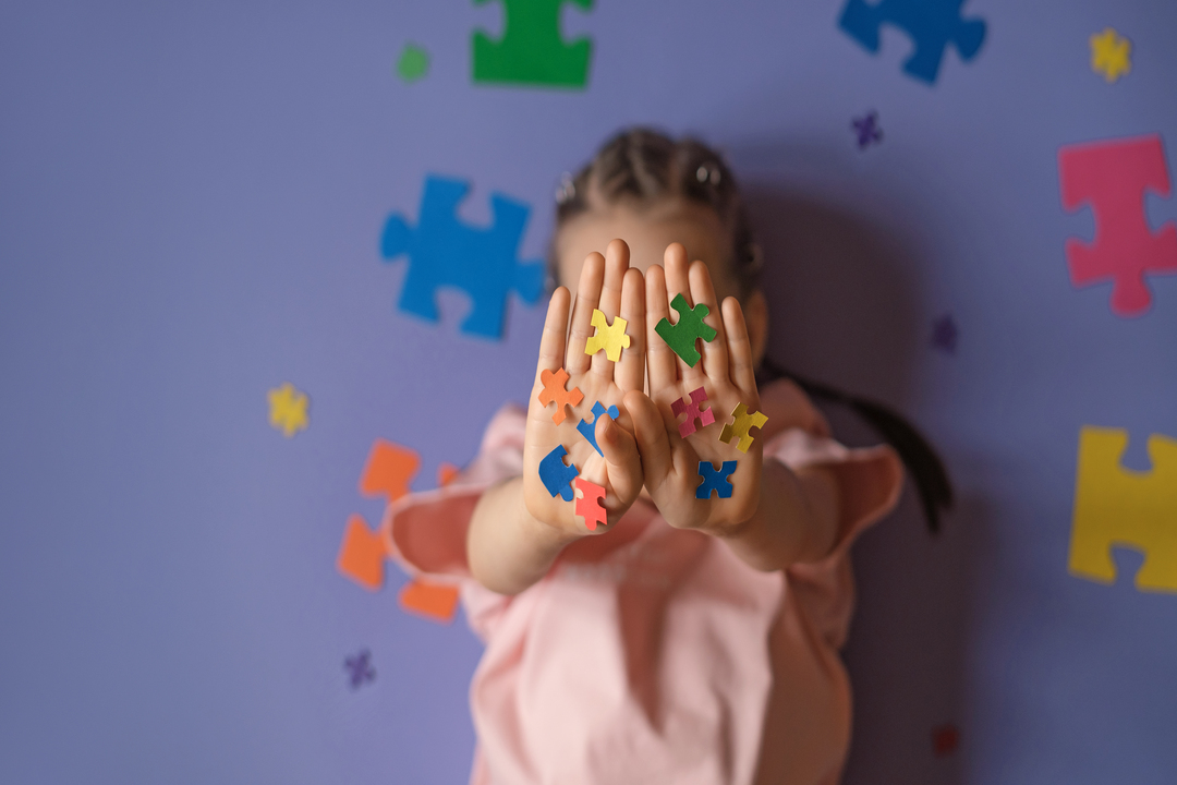 Criança segurando peças coloridas de quebra-cabeça nas mãos, representando o cuidado e o acolhimento no desenvolvimento infantil e no autismo.
