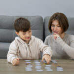 Mãe e criança brincando juntas com cartões sobre a mesa, representando momentos de conexão e acolhimento durante as férias e a quebra de rotina no autismo infantil.