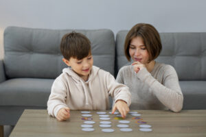 autismo infantil Mãe e criança brincando juntas com cartões sobre a mesa, representando momentos de conexão e acolhimento durante as férias e a quebra de rotina no autismo infantil.