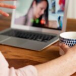 Pessoa segura caneca em videochamada no portátil durante atendimento psicológico online.