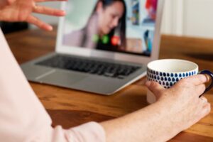 Atendimento psicológico online realmente funciona? Entenda! Pessoa segura caneca em videochamada no portátil durante atendimento psicológico online.