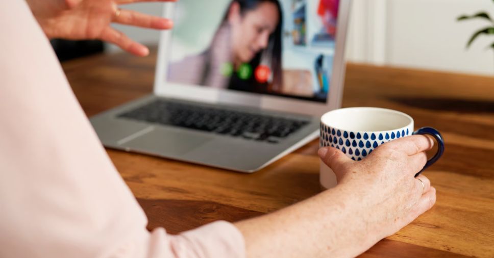 Pessoa segura caneca em videochamada no portátil durante atendimento psicológico online.