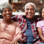 Avós sorriem abraçados às netas no sofá, fortalecendo a relação entre avós e netos.
