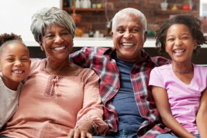 Saiba mais sobre a importância da relação entre avós e netos! Avós sorriem abraçados às netas no sofá, fortalecendo a relação entre avós e netos.