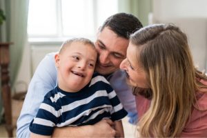 Qual é o papel da família na terapia ABA? Entenda! Pais abraçam e sorriem com o filho para representar a família na terapia ABA.
