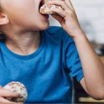 Criança mordendo um biscoito com outro na mão, exemplificando desafios da seletividade alimentar.