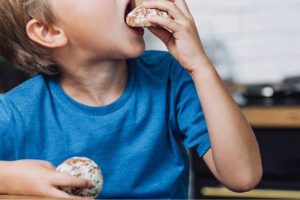 Preferências e recusas de alimentos e seletividade alimentar no autismo Criança mordendo um biscoito com outro na mão, exemplificando desafios da seletividade alimentar.