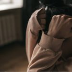 Mulher encolhida com as mãos na cabeça reflete crises de pânico e ansiedade.