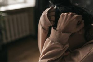 Saiba como a terapia ajuda a controlar crises de pânico e ansiedade. Mulher encolhida com as mãos na cabeça reflete crises de pânico e ansiedade.