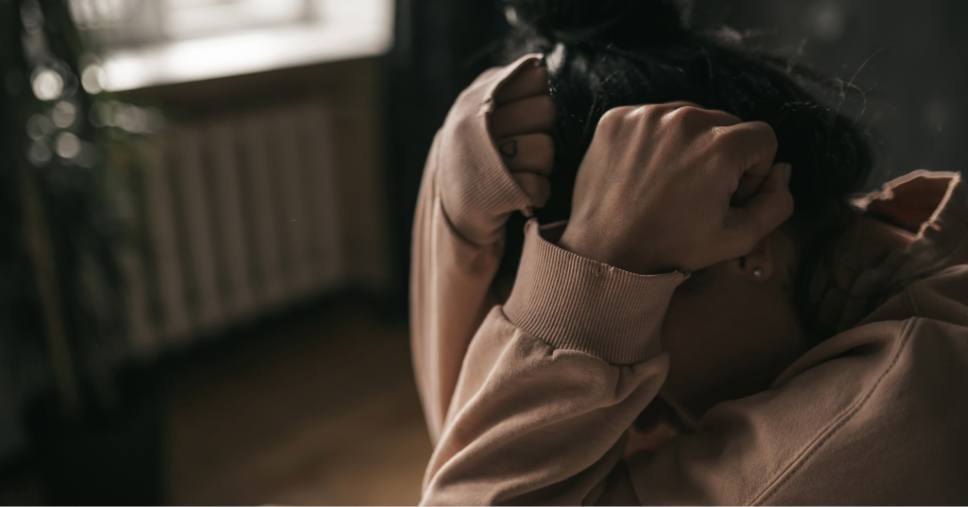 Mulher encolhida com as mãos na cabeça reflete crises de pânico e ansiedade.