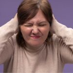 Mulher tapa os ouvidos com expressão de desconforto em crises sensoriais.