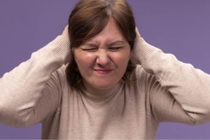 Como a terapia ocupacional pode ajudar nas crises sensoriais? Entenda! Mulher tapa os ouvidos com expressão de desconforto em crises sensoriais.