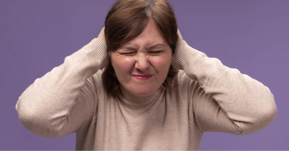 Mulher tapa os ouvidos com expressão de desconforto em crises sensoriais.